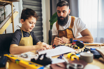 Father teaches his son to plan wood in a carpentry workshop. Hobby and education concept