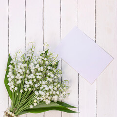 a mockup with a bouquet of lilies of the valley on a white wooden background, a delicate greeting card