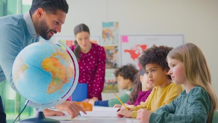 Group of multi-cultural students with teachers in classroom looking at globe in geography lesson - shot in slow motion