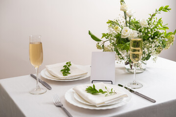 Mockup white blank space card for table number or menu. Wedding teble decoration with white flowers, glasses and white napkins. Elegantly decorated table at a wedding reception. 
