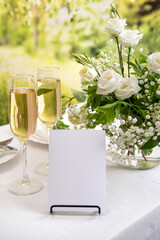Mockup white blank space card for table number or menu. Wedding teble decoration with white flowers, glasses and white napkins. Elegantly decorated table at a wedding reception. 
