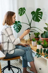Woman spraying houseplant at home, she is caring about her plants. Florist take care of domestic flowers, pour liquid, fertilize, enrich dry ground, horticulture, gardening concept.