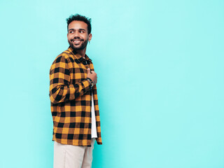 Handsome smiling hipster model. Sexy unshaven man dressed in yellow  summer shirt and jeans clothes. Fashion male posing near blue wall in studio. Cheerful and happy. Isolated