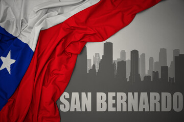 abstract silhouette of the city with text San Bernardo near waving national flag of chile on a gray background.