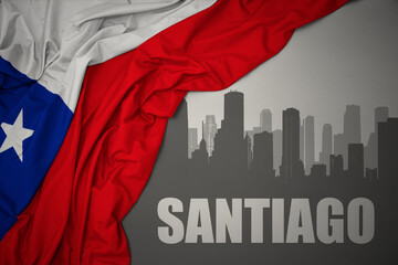 abstract silhouette of the city with text Santiago near waving national flag of chile on a gray background.