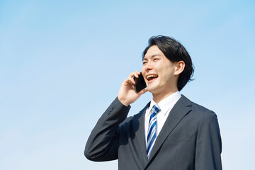 青空背景でスマホで電話する笑顔のビジネスマン