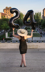 a girl with black balloons, 24 years old, stands with her back in a black dress against the backdrop of the city