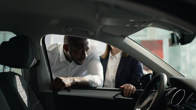 Male client, female manager are studying new car and talking in company spbas. 4k Close view of american african american man exames interior of auto and looks with smile, talks to salesperson and
