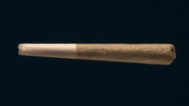 A cannabis pre-roll joint rotating on a black background. Standard pre-roll's components are cannabis, a rolling paper, and a small filter at the end that goes into user mouth.