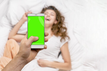 Man taking picture of smiling woman in bed with smartphone and sharing in social network