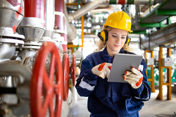 Refinery worker with hardhat and earmuffs checking parameters on tablet computer for oil and gas...