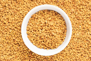 Fenugreek (Trigonella foenum-graecum) in ceramic bowl on background from fenugreek. Macro. Vegetarian food concept
