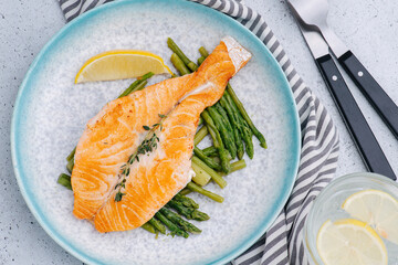 Salmon placed on fried asparagus on a plate with lemon slice.