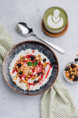 Curd with nuts, raising and jam. On a plate next to a cup of matcha tea