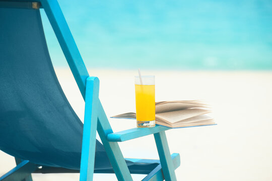 Chair with glass of juice and book on sunny beach, tropical beach vacation and travel conceptvel concept