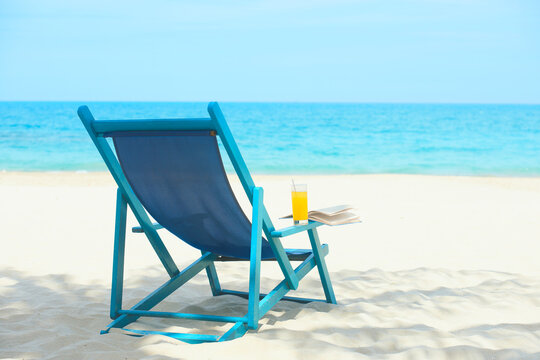 Chair with glass of juice and book on sunny beach, tropical beach vacation and travel concept