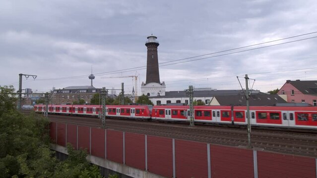 Cologne Ehrenfeld, Germany 2022 - Red commuter train passes with tower in the background on a cloudy day.