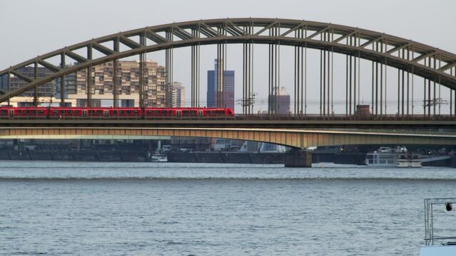 Cologne, Germany 2022:  Train passes the historic Hohenzollern bridge over Rhine river with Crane House in the background on a sunny day.