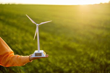 Person holds toy wind generator on green field background on sunset, close-up. Concept of...