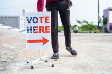 Man placing vote here sign board direction near polling booth - concept of responsibility, voting...