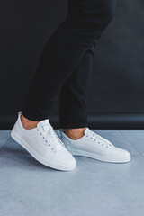 A man in white leather casual sneakers, summer men's sneakers. Man in black jeans
