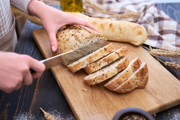 Woman cutting freshly baked bread at wooden kitchen table