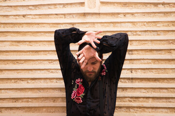 Portrait of a man dancing flamenco with a black shirt and red roses, on a brown background doing different postures with his hands. Feel passion. Flamenco dance concept cultural heritage of humanity.