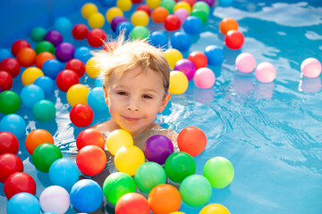 Fototapeta na wymiar Young child, swimming in the summer in a pool full of colorful balls, enjoying beautiful sunny weather