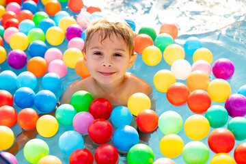Fototapeta na wymiar Young child, swimming in the summer in a pool full of colorful balls, enjoying beautiful sunny weather