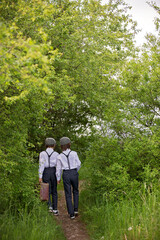 Sweet children in vintage clothing, hat, suspenders and white shirts, holding suitcase, running in the park