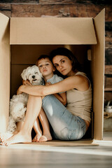 Mother, holding her toddler child in her arms, sitting in cardboard box