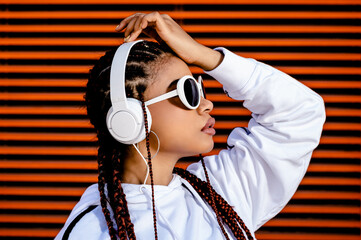 Young African American woman with braided hair wearing urban sportswear with headphones and...
