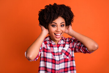 Portrait of cheerful excited person hands touch wavy hairdo toothy smile isolated on orange color background