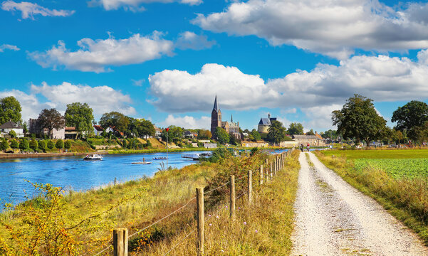 Beautiful dutch rural countryside landscape, riverside waterfront bike cycle path to ferry station, medieval town church tower, river Maas - View from Beesel on Kessel, Netherlands, Limburg