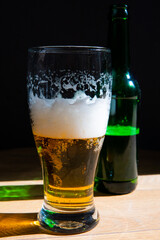 beer in a glass near a green bottle and on a black background