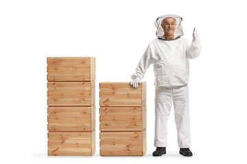 Full length portrait of a male bee keeper standing with wooden boxes and gesturing thumbs up