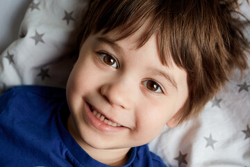Portrait of happy 5 year child. Little boy lays on the bed and smile. Close-up smiling baby face. Cute caucasian appearance. Happy childhood. Home lifestyle. Brown hair and big beautiful brown eyes