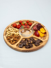 wooden bowl filled with fruits, nuts, strawberries, chocolate on a white background. Picnic in nature