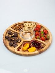 wooden bowl filled with fruits, nuts, strawberries, chocolate on a white background. Picnic in nature