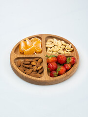 wooden bowl filled with fruits, nuts, strawberries, chocolate on a white background. Picnic in nature
