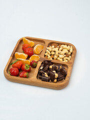 wooden bowl filled with fruits, nuts, strawberries, chocolate on a white background. Picnic in nature