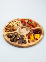 wooden bowl filled with fruits, nuts, strawberries, chocolate on a white background. Picnic in nature