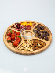 wooden bowl filled with fruits, nuts, strawberries, chocolate on a white background. Picnic in nature