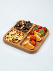 wooden bowl filled with fruits, nuts, strawberries, chocolate on a white background. Picnic in nature