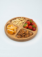 wooden bowl filled with fruits, nuts, strawberries, chocolate on a white background. Picnic in nature