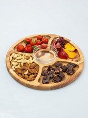 wooden bowl filled with fruits, nuts, strawberries, chocolate on a white background. Picnic in nature
