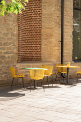 Fototapeta na wymiar Cafe or restaurant terrace with empty yellow chairs and tables. Summer open air service. Eating outside on warm, sunny day. European street view. Hipster style, modern, futuristic furniture. Vertical