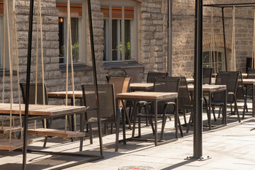 Cafe or restaurant terrace with empty chairs and tables. Summer open air. Eating outside on warm, sunny day. European street view. Hipster style, modern wooden furniture, swing instead of chair