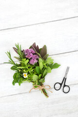 Herbs tied in a bunch for food seasoning and used in herbal plant based medicine for various illnesses. Health care concept on rustic white wood background with scissors, flat lay, top view.
