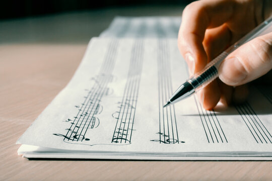 Handwritten notes and female hand holding a pen and writing notes, composing music, selective focus